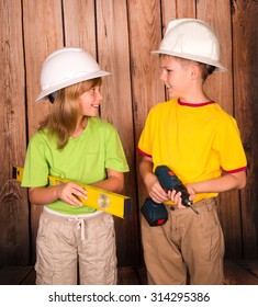 Smiling children in hardhats with tools on wooden background looking at each other. Renovation and construction concept. 