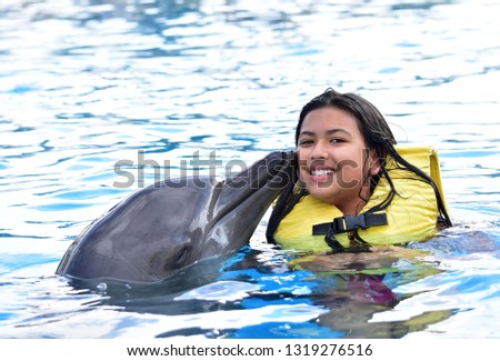 Smiling children kissing dolphin in pool.