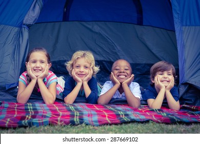 Smiling children lie down in the tent together in the park on a sunny day