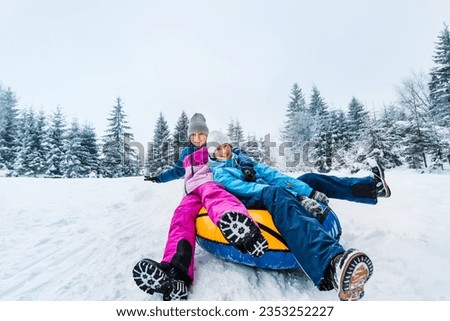 Smiling children ride down on inflatable tubing sleds. Inflatable sleds for active winter family recreation. Wide angle shooting.