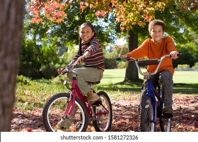 Smiling children riding bikes in autumn park at camera