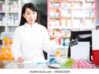 Smiling chinese female pharmacist standing with a cash desk in drugstore