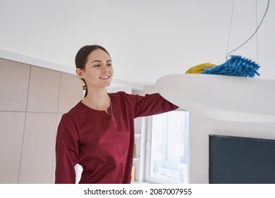 Smiling Cleaning Woman Dusting Ceiling Light Fixture