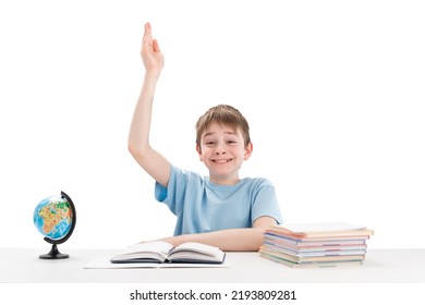 Smiling Clever Schoolboy Raised His Hand During The Lesson. Excellent Student Knows The Answer. Portrait Of Boy At The Table.