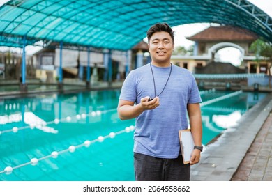 Smiling Coach Holding Clipboard And Stopwatch While Standing