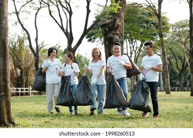 Smiling College Students Volunteering In City Park Or On Campus And Collecting Garbage In Big Trash Bags