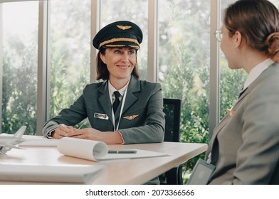 Smiling Commercial Female Pilot Provides Training To Young Flight Crew. Beautiful Middle Aged Woman Airplane Captain Instructor Has A Meeting, Discussion With Aircrew Team. Aviation Business Concept