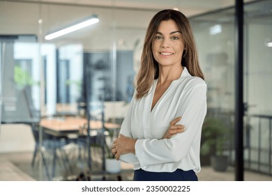 Smiling confident 45 years old Latin professional middle aged business woman corporate leader, happy mature female executive, lady manager standing in office arms crossed looking at camera, portrait. - Powered by Shutterstock