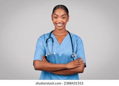 Smiling confident black millennial doctor surgeon, nurse in blue uniform with crossed arms on chest, isolated on gray studio background. Medical ad and offer, health care, professional help, advice