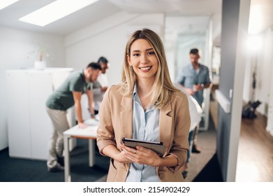 Smiling confident business leader looking at camera and standing in an office at team meeting. Portrait of confident businesswoman with colleagues in boardroom. Posing while holding digital tablet. - Shutterstock ID 2154902429
