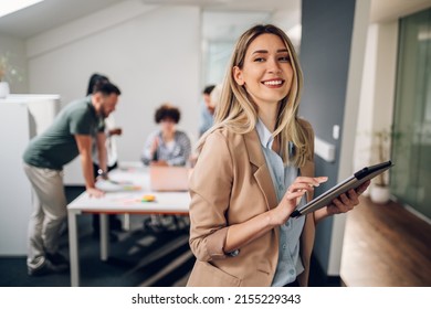 Smiling confident business leader looking at camera and standing in an office at team meeting. Portrait of confident businesswoman with colleagues in boardroom. Using digital tablet during a meeting. - Shutterstock ID 2155229343