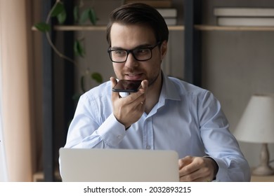 Smiling Confident Business Man Recording Audio Message On Mobile Phone, Giving Vocal Command To Virtual Assistant For Online Search, Using Voice Recognition App, Speaking At Speaker At Workplace