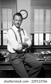 Smiling confident businessman sitting on vintage office desk.