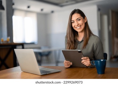 Smiling confident businesswoman looking at camera sitting at home office desk. Modern stylish female manager, successful female entrepreneur holding digital tablet posing for business portrait.
 - Powered by Shutterstock