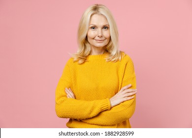 Smiling confident elderly gray-haired blonde woman lady 40s 50s years old in yellow casual sweater stand holding hands crossed looking camera isolated on pastel pink color background studio portrait - Powered by Shutterstock