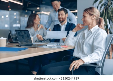 Smiling Confident Female Boss Sitting On Meeting And Looking At Side With Her Colleagues At Background In Office. Business Concept