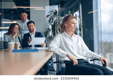 Smiling Confident Female Boss Sitting On Meeting And Looking At Side With Her Colleagues At Background In Office. Business Concept