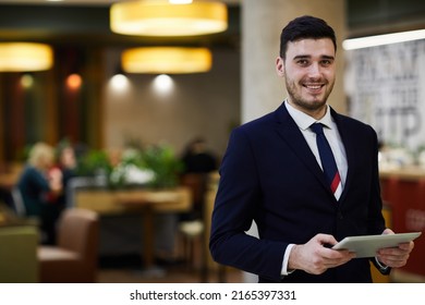 Smiling Confident Handsome Young Male Manager Of Restaurant Wearing Suit Using Digital Tablet For Inserting Data, He Looking At Camera