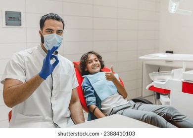 Smiling confident male dentist showing okay gesture while his patient kid boy smiling with thumb up after tooth teeth braces correction - Powered by Shutterstock