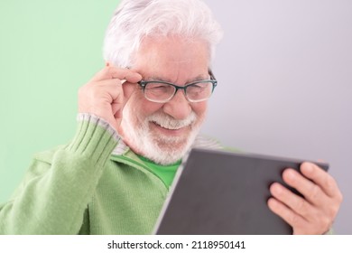 Smiling Confident Male Teacher With A Tablet-pc Held In His Hands Standing On Cute Background. White-haired Mature Caucasian Man With Glasses, College Student Of The Third Age University