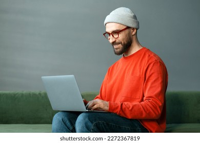 Smiling confident man programmer using laptop computer, typing on keyboard working freelance project sitting at workplace. Modern bearded hipster watching training courses, planning startup in office 
