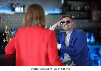 Smiling confident man in sunglasses meets woman near bar counter. Narcissistic personality disorder in men concept - Shutterstock ID 2364686741