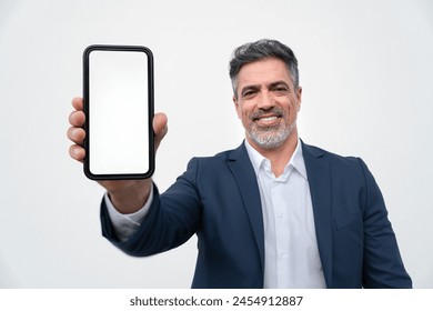 Smiling confident mature businessman showing mobile phone blank white screen mockup to camera standing isolated on background. Man in suit holding smartphone for finance business bank advertising app - Powered by Shutterstock