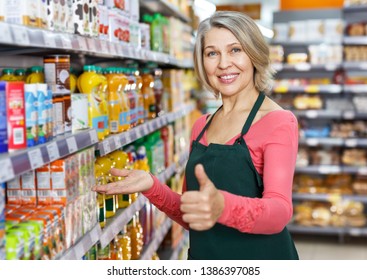 Smiling confident mature saleswoman giving thumbs up, recommending quality food products at supermarket  - Powered by Shutterstock