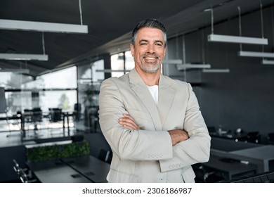 Smiling confident middle aged business man, mature older professional successful company ceo corporate leader wearing beige suit standing in modern office arms crossed looking at camera, portrait.
