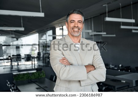 Smiling confident middle aged business man, mature older professional successful company ceo corporate leader wearing beige suit standing in modern office arms crossed looking at camera, portrait.