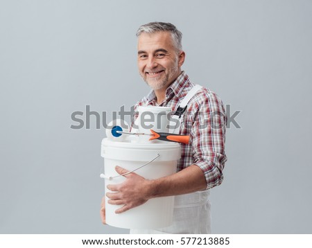 Smiling confident painter and decorator posing with a paint roller and buckets, he is looking at camera