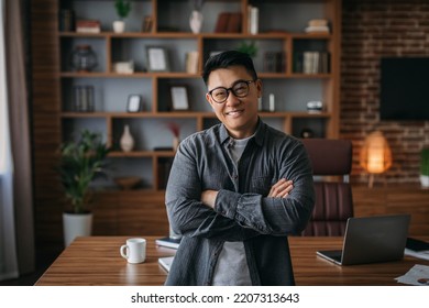 Smiling Confident Successful Adult Chinese Man In Glasses With Crossed Arms On Chest Looking At Camera In Office Interior. Businessman At Work At Home, Development And Business, Trading And Marketing