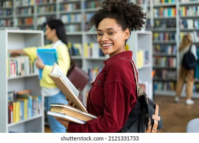 Smiling confident teen girl college student looking at camera. Happy multiracial woman wearing glasses posing in library classroom. Close up headshot portrait 