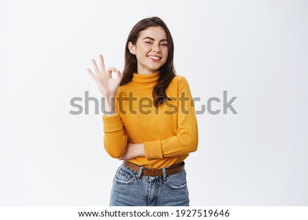 Smiling confident woman assure and guarantee all good, showing okay sign, have situation under control, like and praise promo offer, white background.