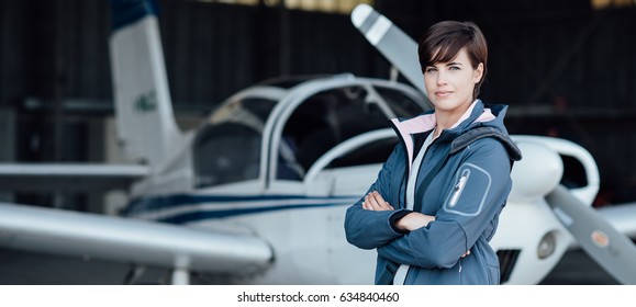 Smiling confident woman posing with her airplane in the hangar before departure, aviation and light aircrafts concept