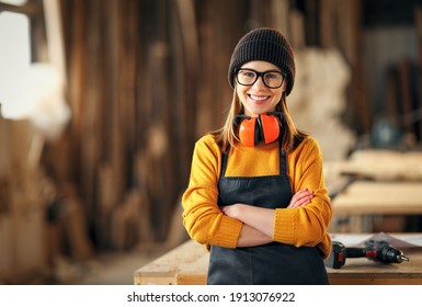 Smiling confident young female joiner in apron standing near workbench and looking at camera friendly while working in craft workshop - Powered by Shutterstock