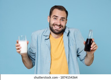 Smiling confused young bearded man guy 20s wearing casual clothes posing holding in hands glass of milk bottle of cola looking camera isolated on pastel blue color wall background studio portrait