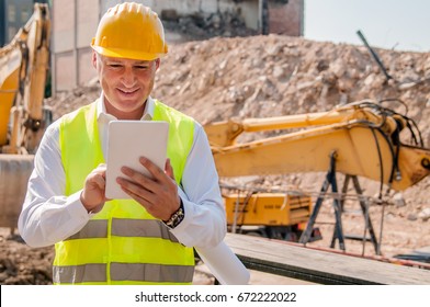 Smiling Construction Manager Standing On Building Site. Builder Worker Activity With Digital Tablet On Construction Site