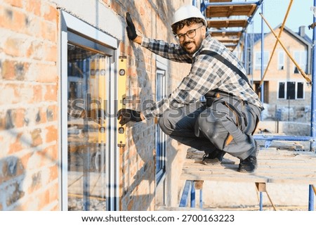 Smiling construction worker installing a window, checking alignment with a spirit level on a building site