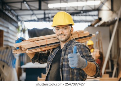 Smiling construction worker in a yellow hardhat and plaid shirt holding wood planks on his shoulder and thumb up finger. Ideal for carpentry, woodworking in furniture workshop, National Carpenters Day - Powered by Shutterstock