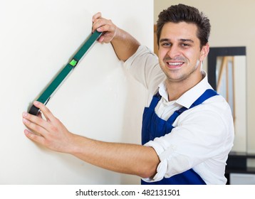 Smiling constructor smoothing the wall surface indoors