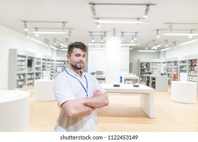 Smiling Is A Consultant On The Background Of Modern Light Technology Store. Portrait Of A Handsome Man Seller In An Electronics Store.