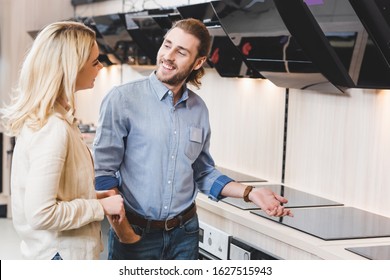 smiling consultant talking with woman near cooker hoods and cookers in home appliance store