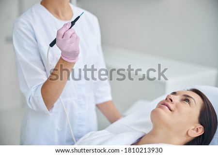 Smiling contented adult Caucasian female patient with dark hair looking upward during the electrosurgical procedure