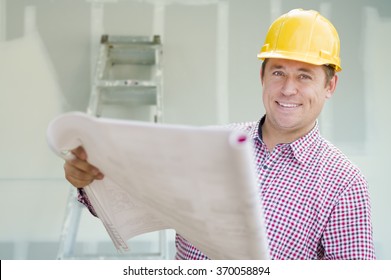 Smiling Contractor Holding Blueprints Inside Home Construction Site.