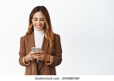 Smiling corporate woman order taxi in app, chatting in messanger app on smartphone, looking at her phone screen with pleased face, white background