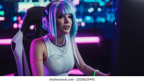 Smiling Cosplay Girl Talking to Her Online Friends on Desktop Computer While Sitting in Futuristic Cyberpunk Home. Young Female Playing Internet Video Game with Other Players