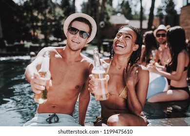 Smiling Couple With Alcoholic Drinks At Poolside. Beautiful Black Woman And Young Man Holding Bottles Of Beer And Having Fun At Poolside. Happy Friends Enoying Pool Party. Summer Vacation Concept