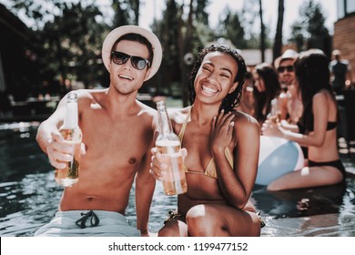 Smiling Couple With Alcoholic Drinks At Poolside. Beautiful Black Woman And Young Man Holding Bottles Of Beer And Having Fun At Poolside. Happy Friends Enoying Pool Party. Summer Vacation Concept