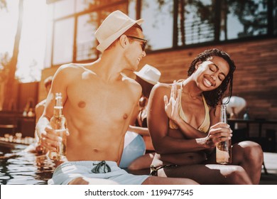 Smiling Couple With Alcoholic Drinks At Poolside. Beautiful Black Woman And Young Man Holding Bottles Of Beer And Having Fun At Poolside. Happy Friends Enoying Pool Party. Summer Vacation Concept